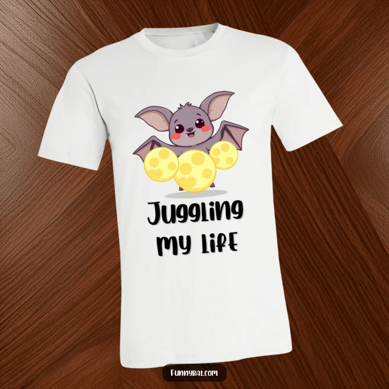 Funny t-shirt showing a plump bat with happy eyes trying to juggle large, luminous moons, representing joyful effort.
